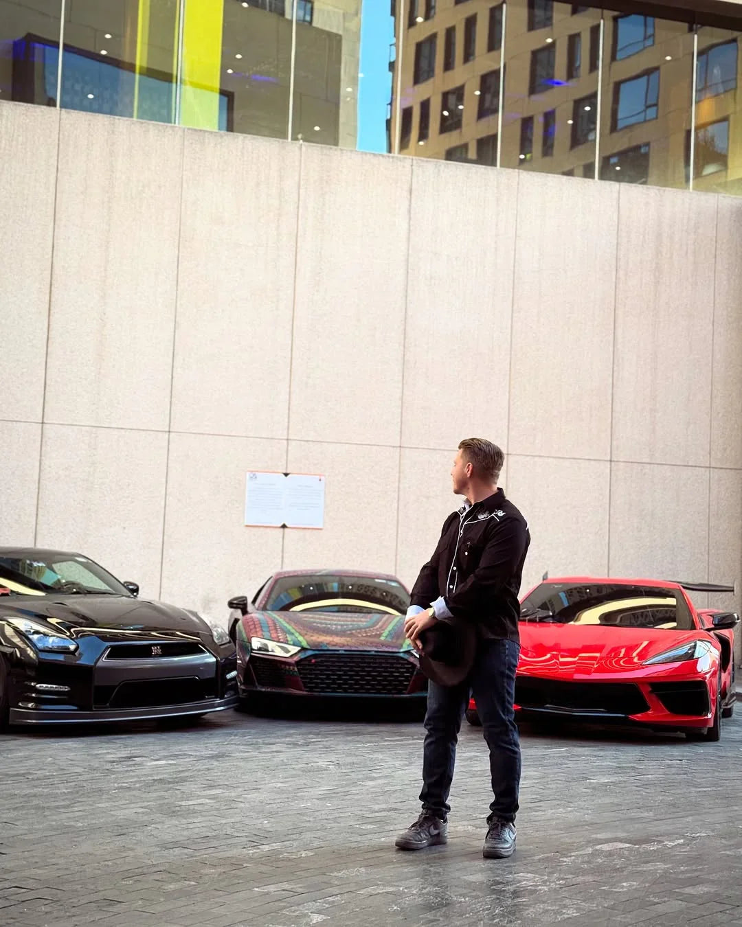 Hombre de pie frente a autos deportivos importados, fondo urbano, Carmexio México